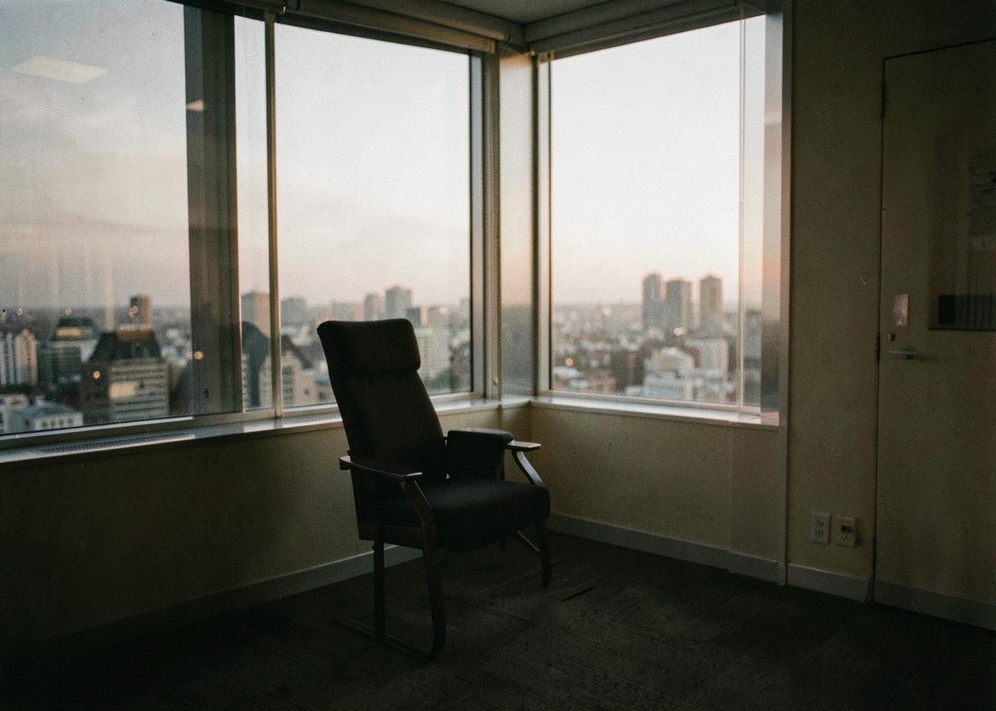 Une pièce calme avec un fauteuil face à une grande baie vitrée ouverte sur la ville au crépuscule