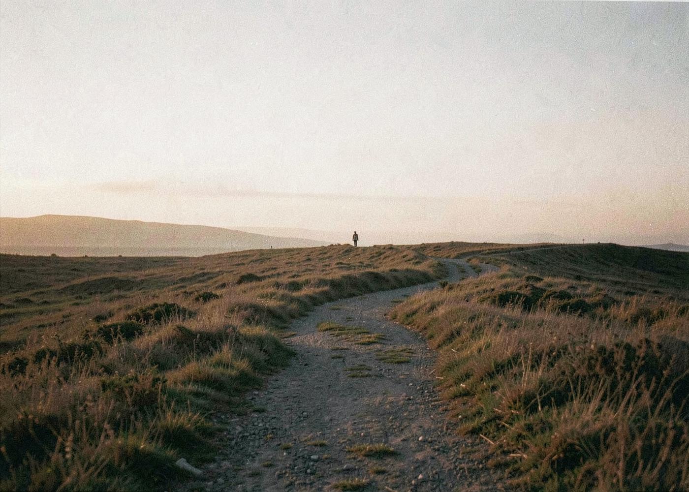 Un chemin sinueux dans un paysage ouvert au lever du jour, une silhouette au loin